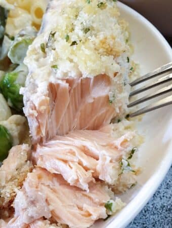 A piece of salmon topped with cheesy breadcrumbs being flaked with a fork.