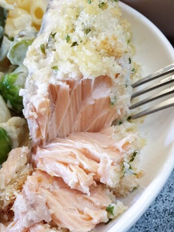 A piece of salmon topped with cheesy breadcrumbs being flaked with a fork.