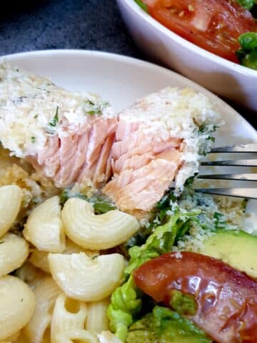 A piece of salmon topped with cheesy breadcrumbs being flaked with a fork.