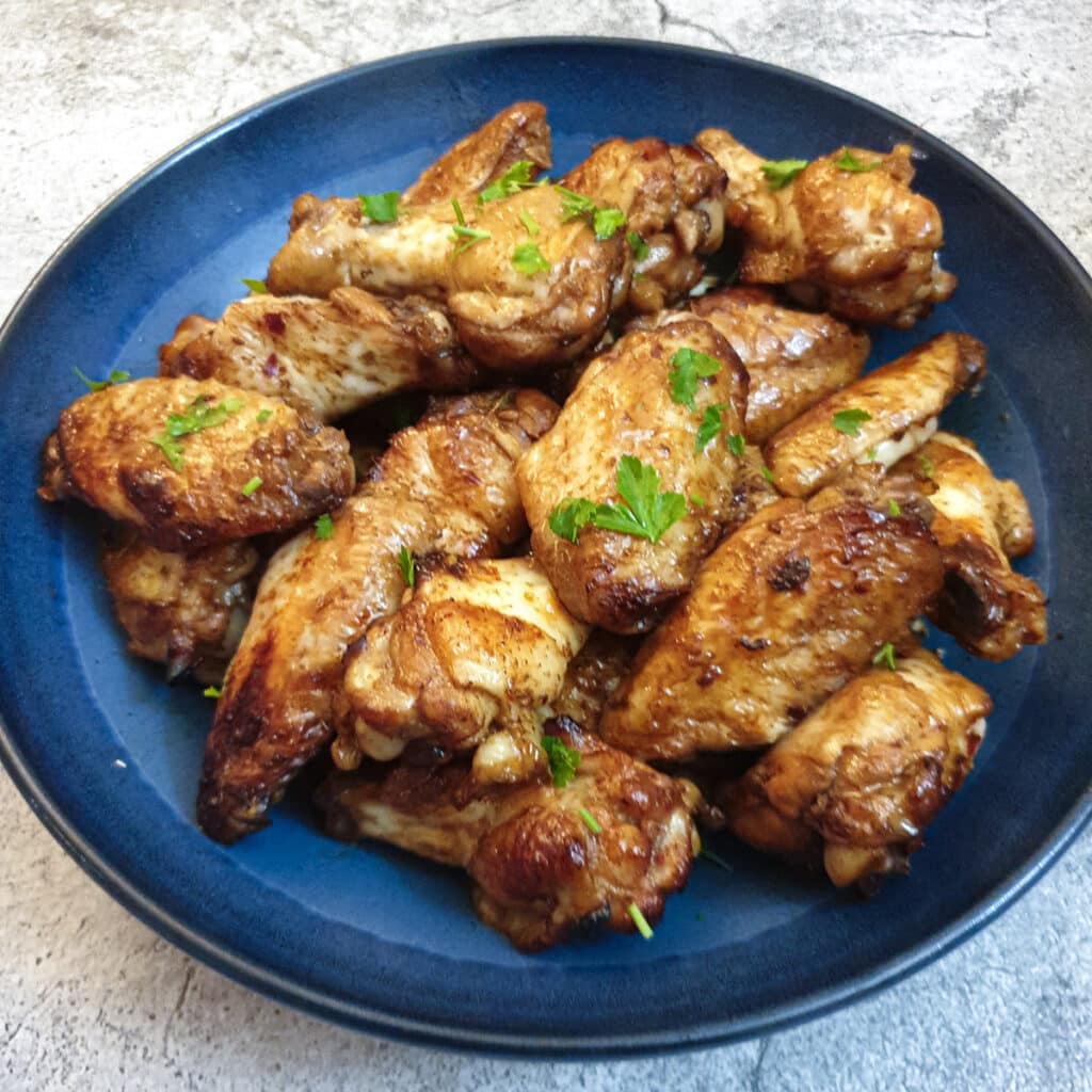 A pile of sticky chicken wings in a blue serving dish.