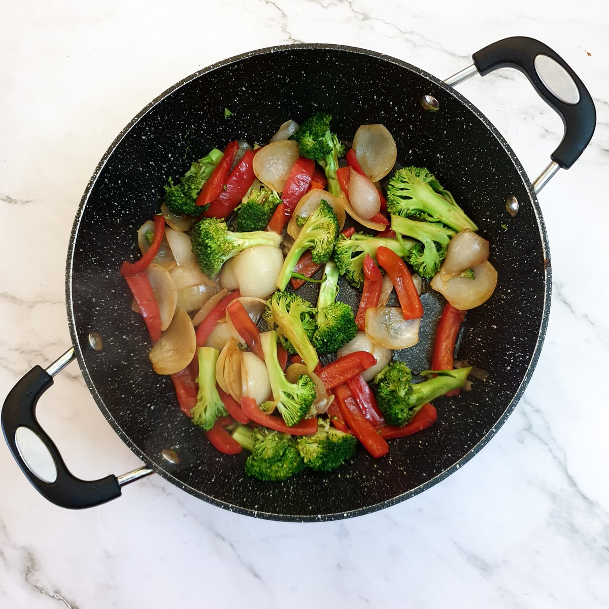 Broccoli florets added to onions and red peppers in a frying pan.