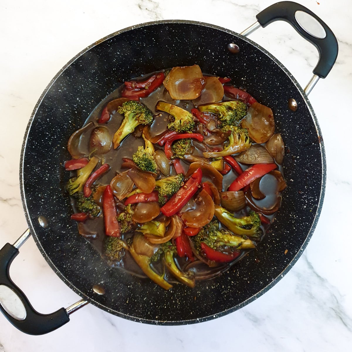 Sauce stirred through the onions, red peppers and broccoli in a frying pan.