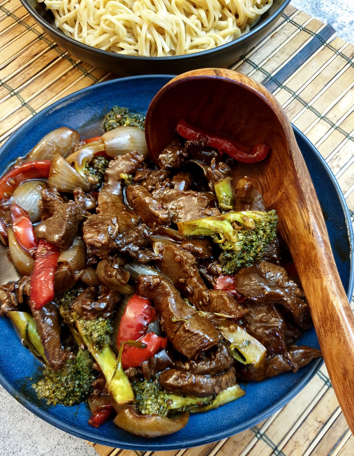 A blue dish filled with Szechuan beef stir fry with a wooden serving spoon.