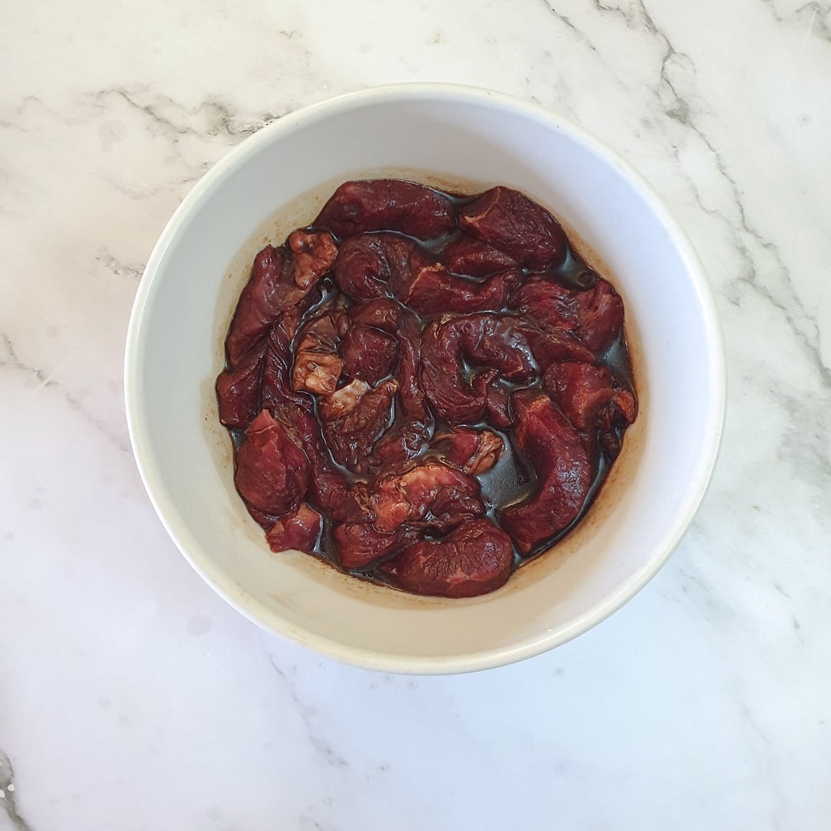 Beef strips marinating in a white bowl.