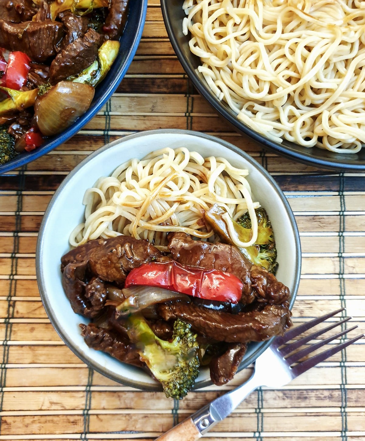 A small white dish holding noodles and a helping of Szechuan beef stirfry.