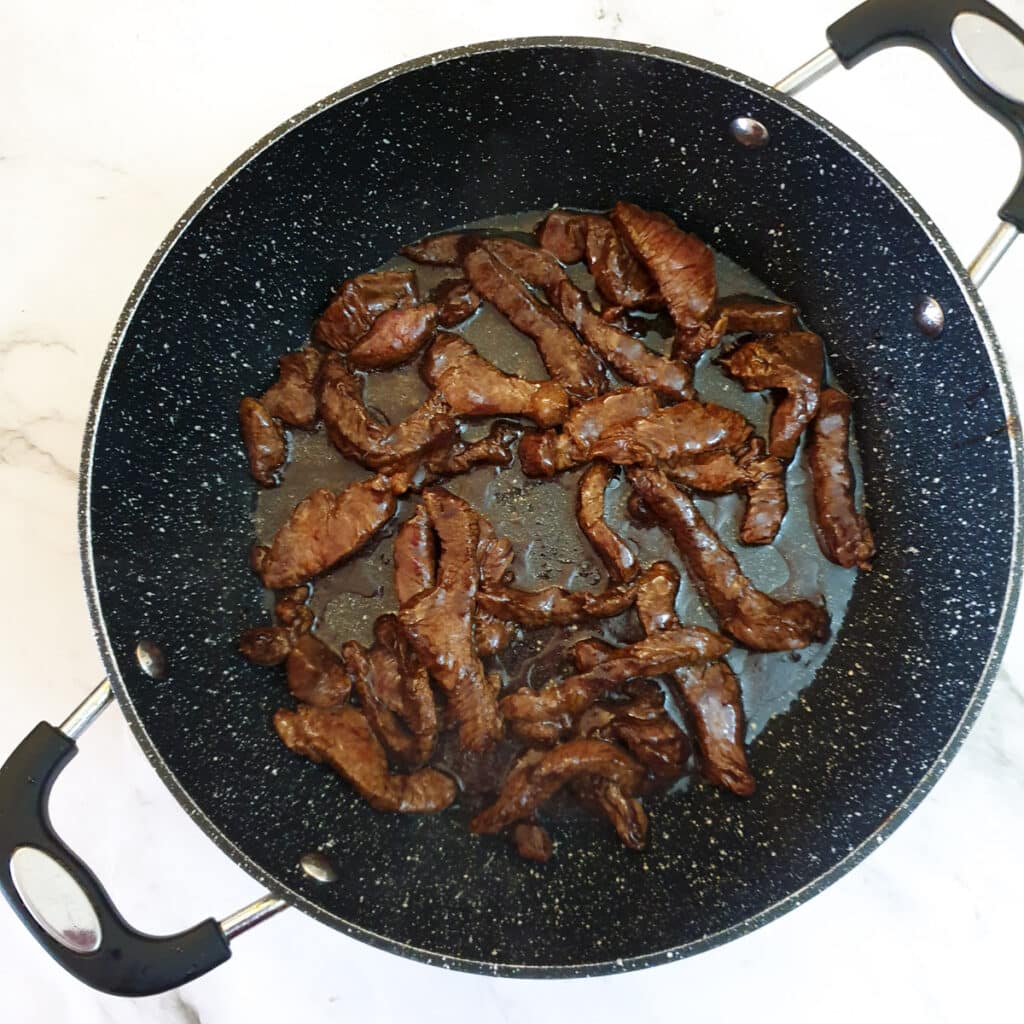 Beef strips frying in a frying pan.