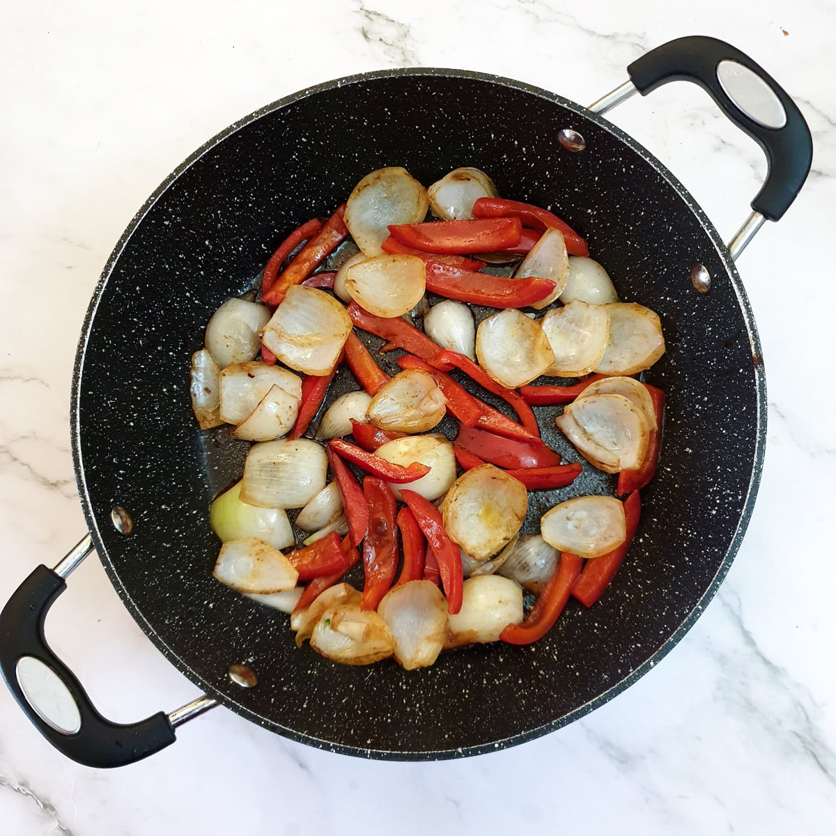 Onions and red peppers in a frying pan.