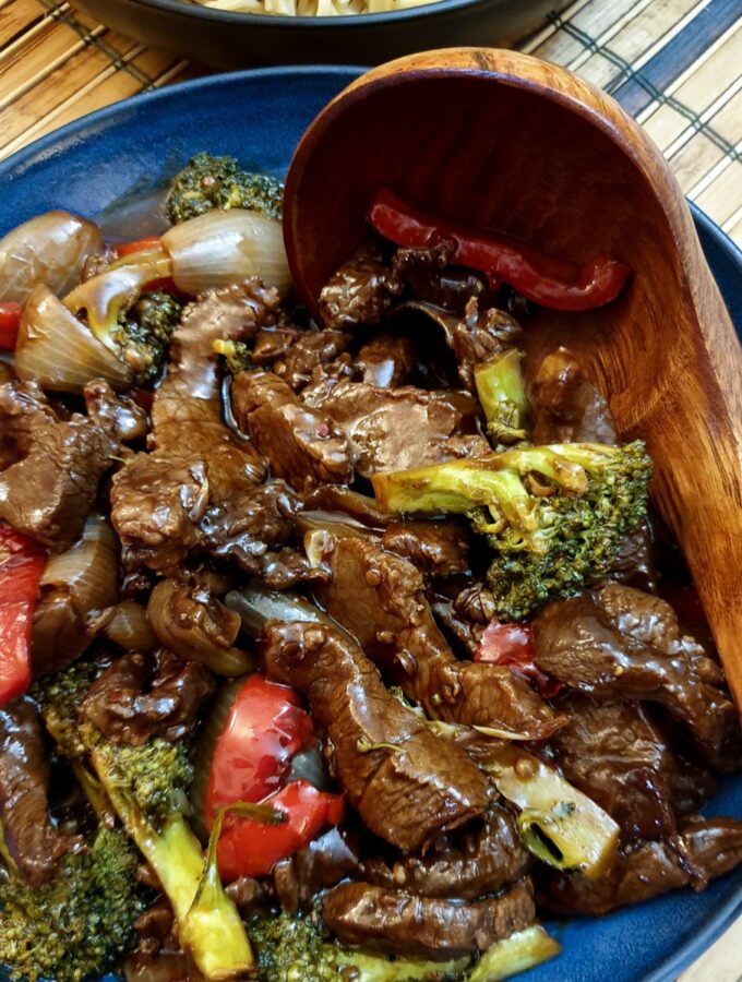 A blue dish filled with Szechuan beef stir fry with a wooden serving spoon.