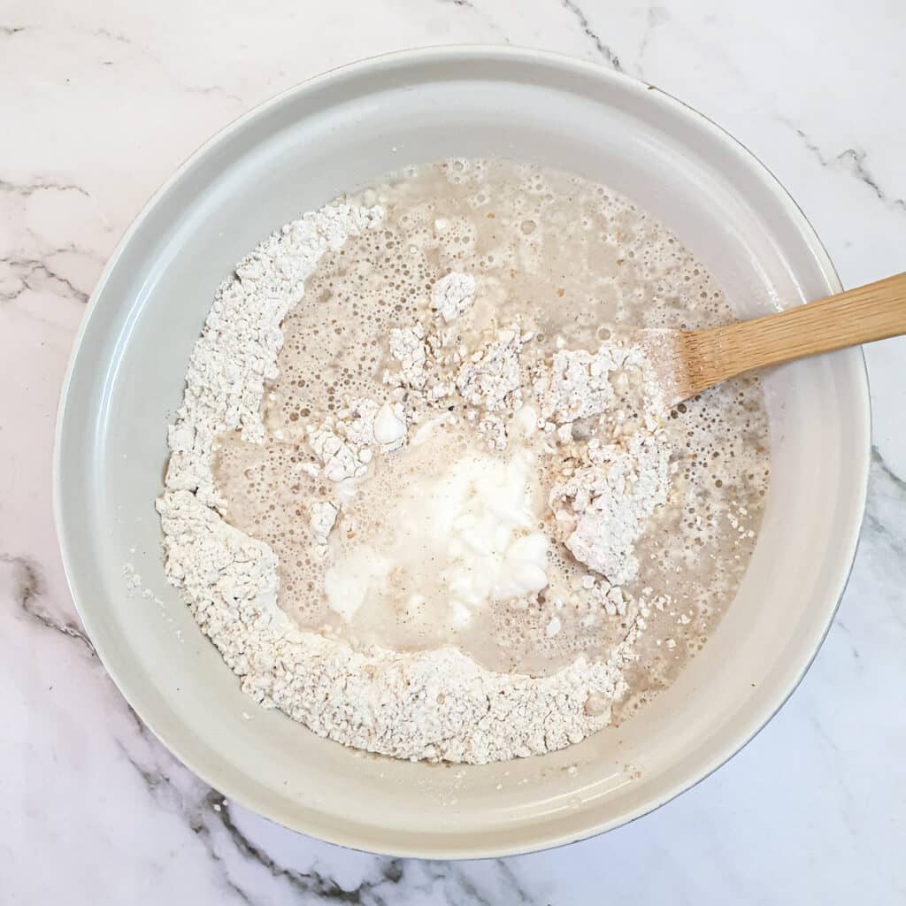Water and yoghurt added to flour and oats in a mixing bowl.