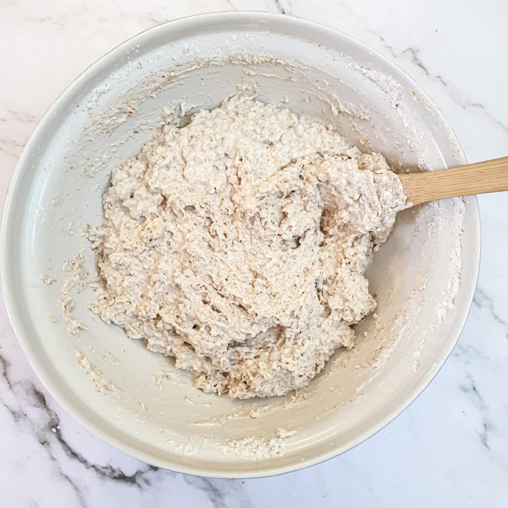 Seeded bread roll dough mixed to a sticky ball in a mixing bowl.