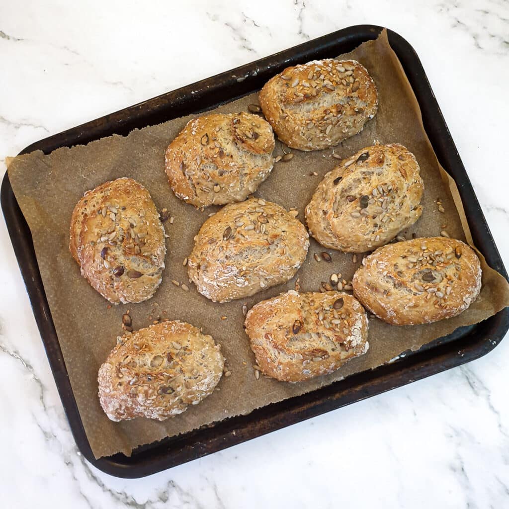 8 baked seeded breadrolls on a baking tray.