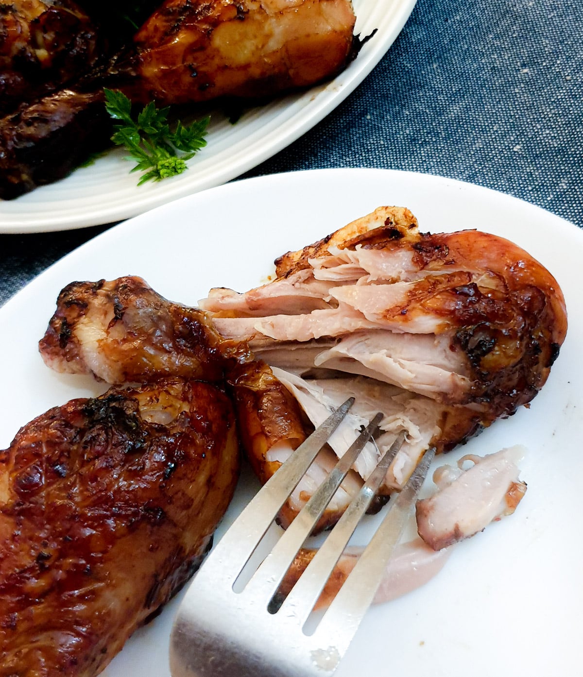 A chicken drumstick on a white plate being pulled open with a fork to show the juicy texture.