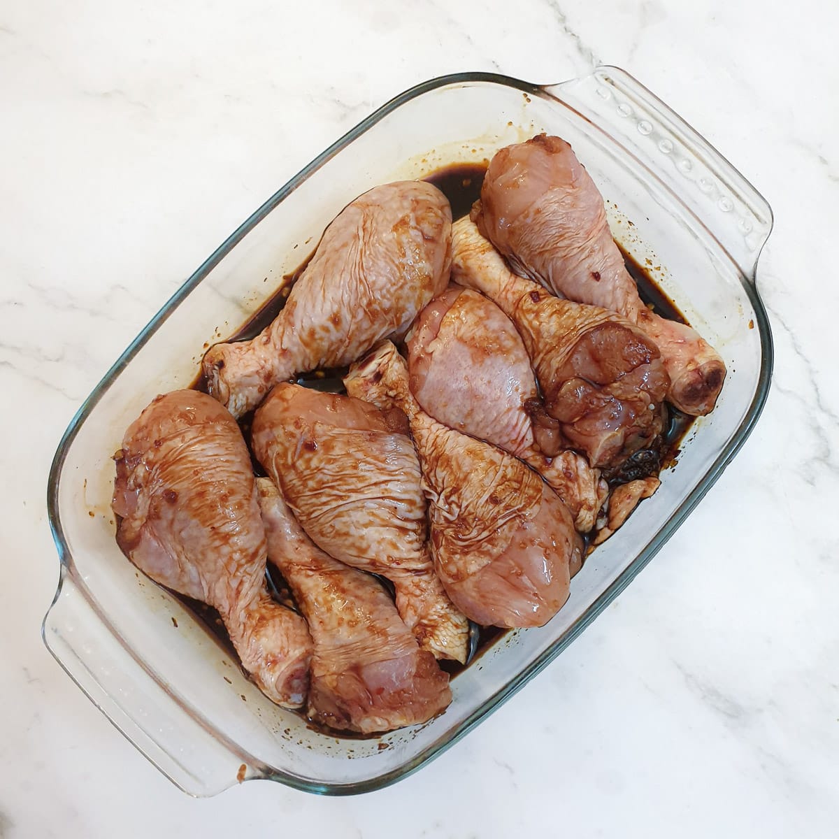 8 chicken drumsticks marinating in a glass dish.