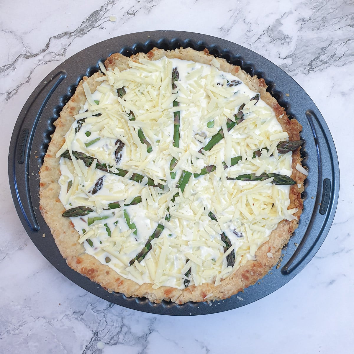 A cheese and asparagus quiche covered with grated cheese, ready to be baked.