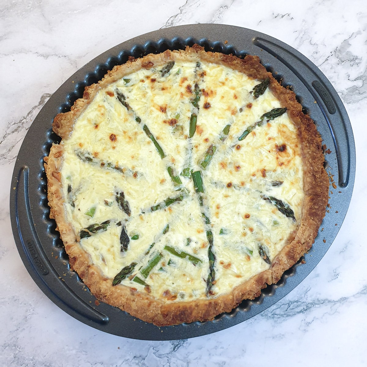 Overhead shot of a baked cheese and asparagus quiche in a flan dish.