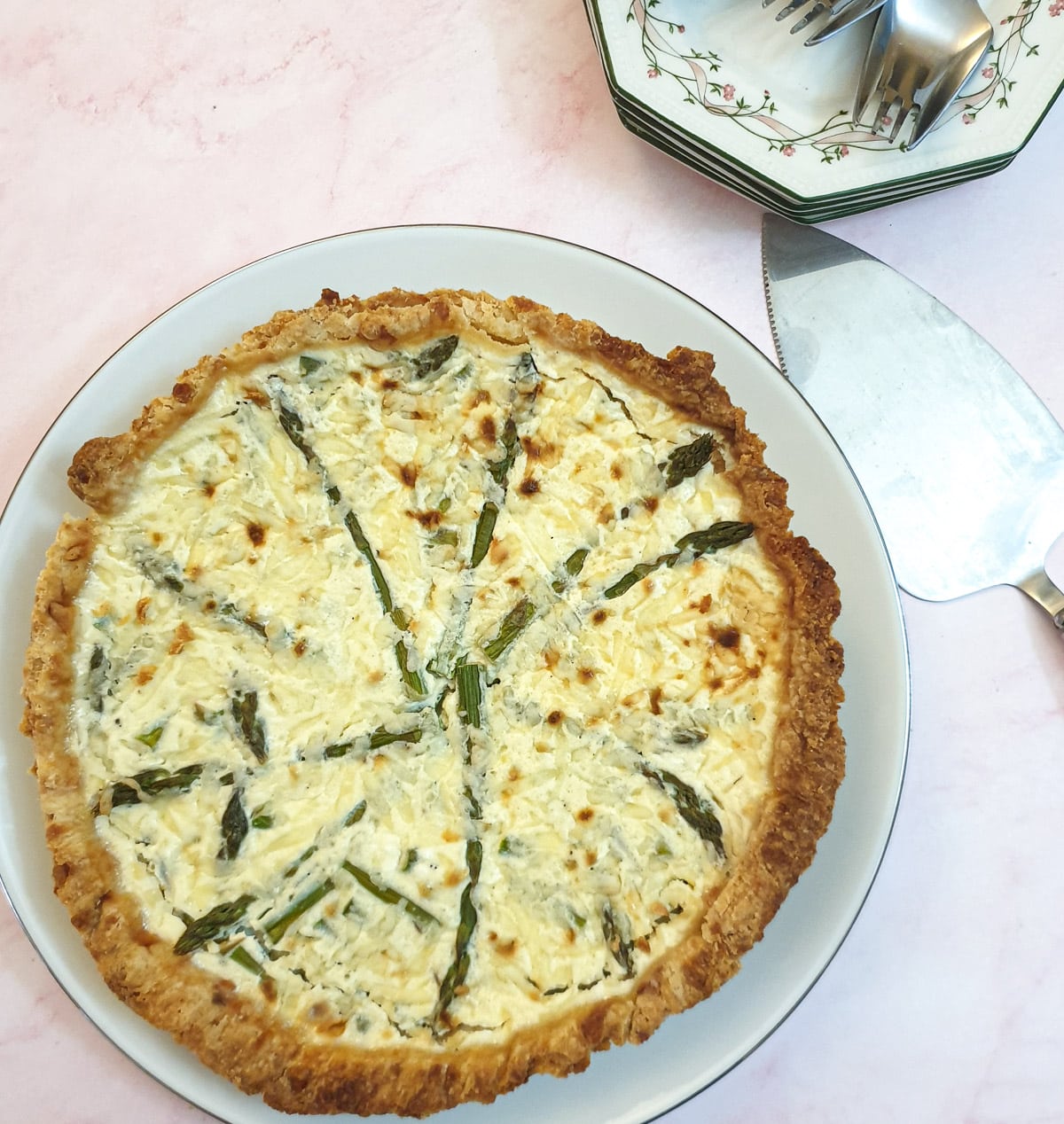 Overhead shot of a cheese and asparagus quiche on a white plate.