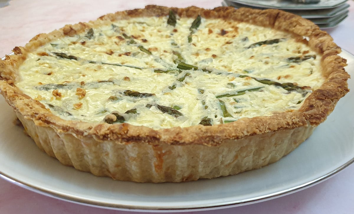 Side on view of a cheese and asparagus quiche on a white plate.