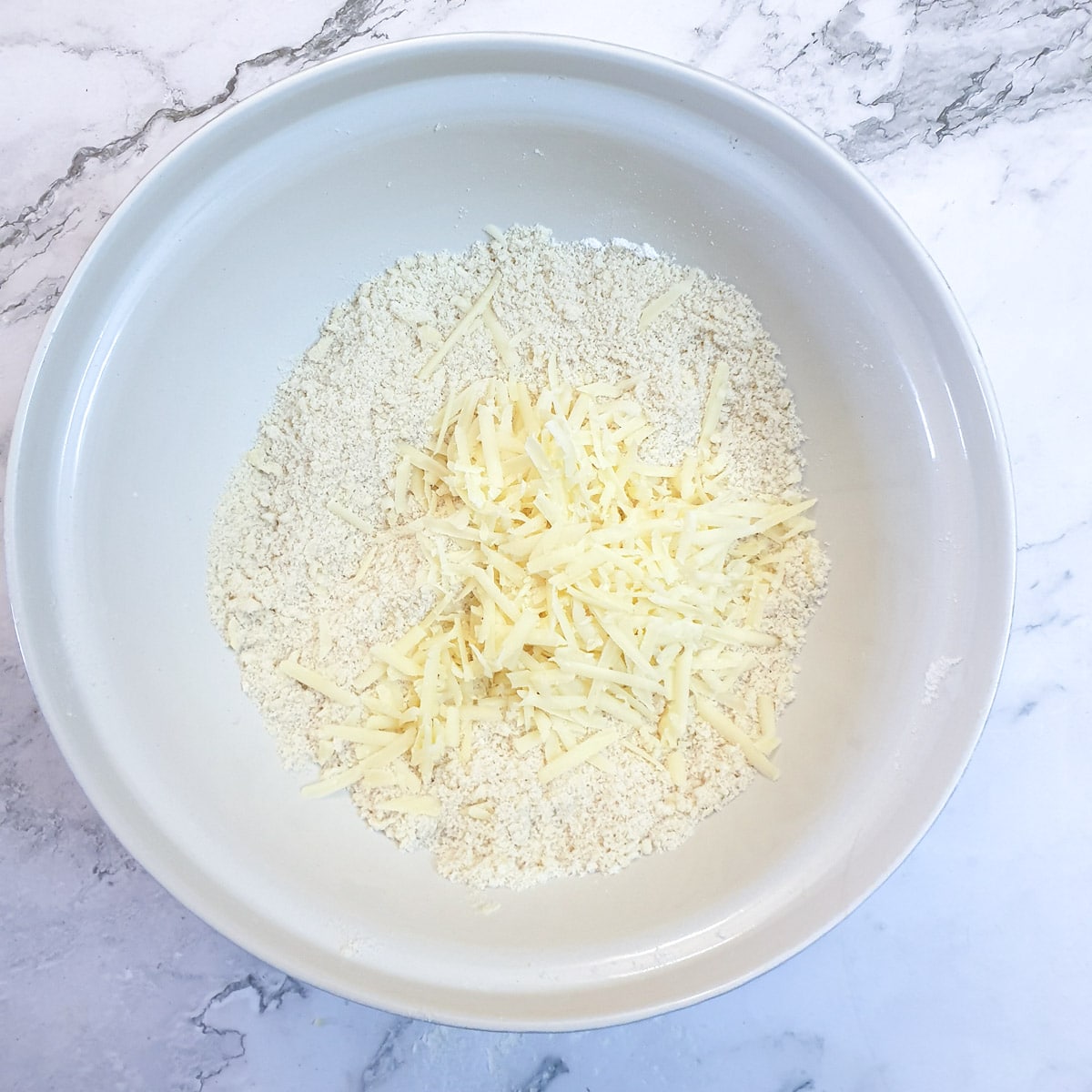 A mixing bowl containing rubbed in flour and butter and grated cheese.