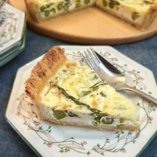 A slice of cheese and asparagus tart on a green patterned plate with a fork.