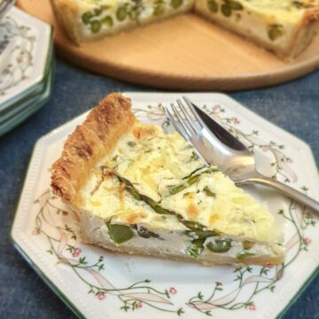 A slice of cheese and asparagus tart on a green patterned plate with a fork.