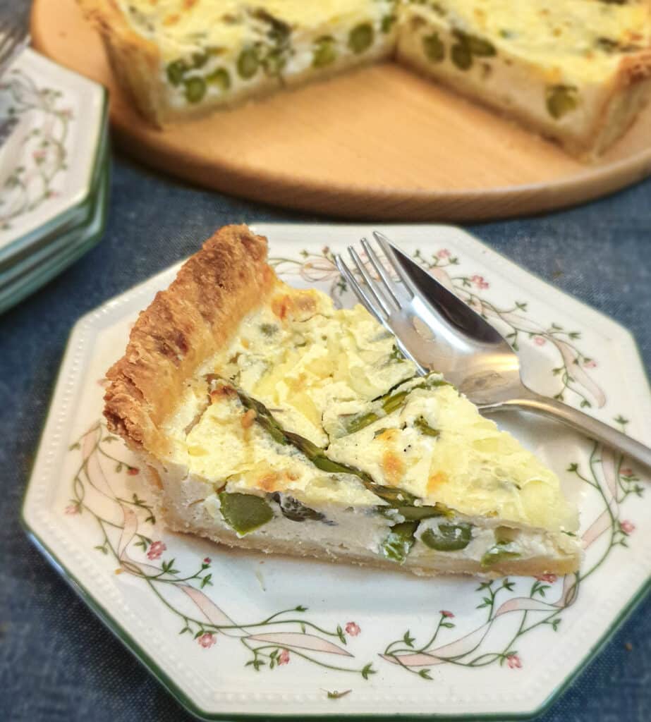 A slice of cheese and asparagus tart on a green patterned plate with a fork.