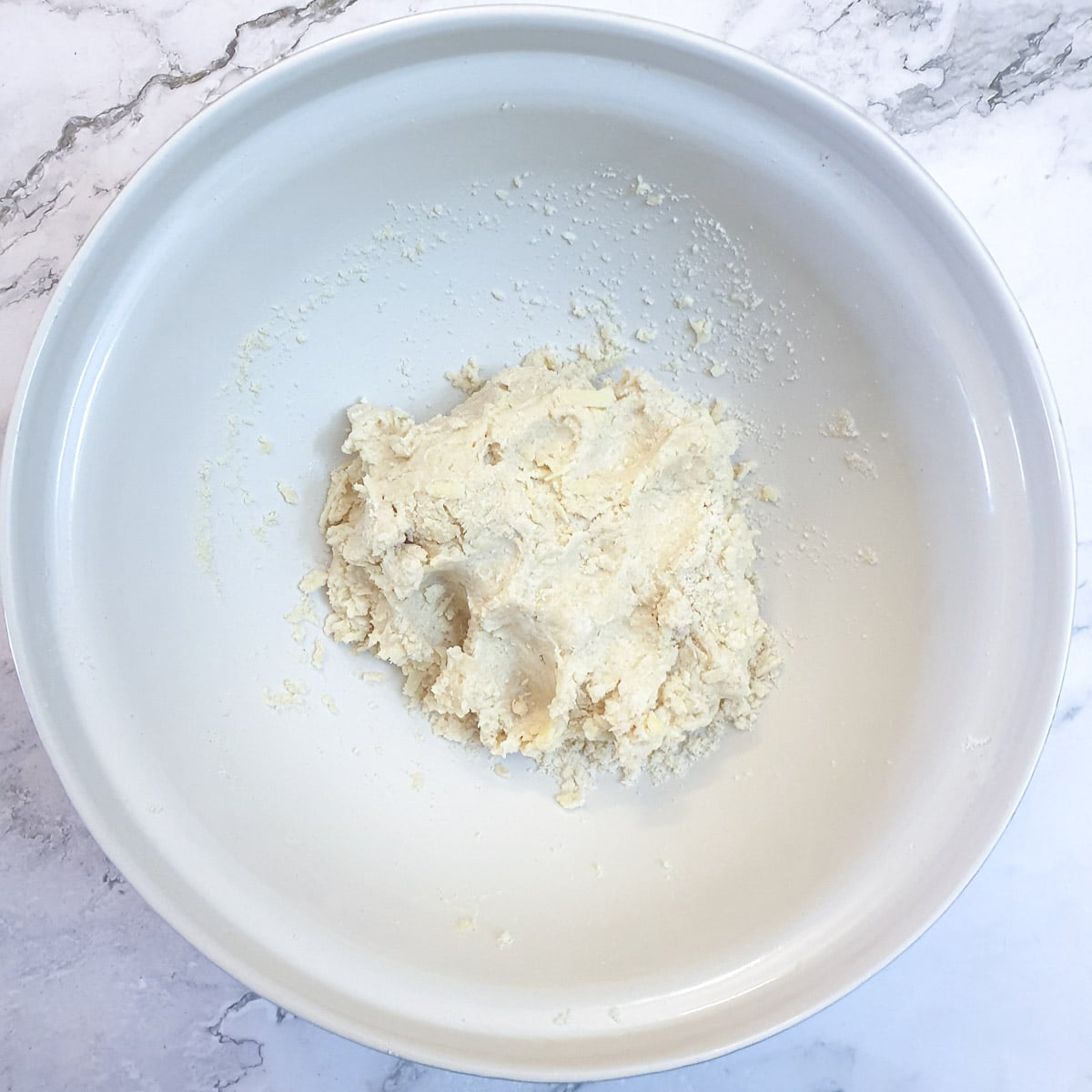 A mixing bowl with a ball of dough that has been brought together with water.