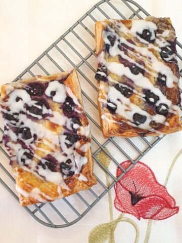 2 blueberry cream cheese danish pastries drizzled with a sweet glaze on a cooling rack.
