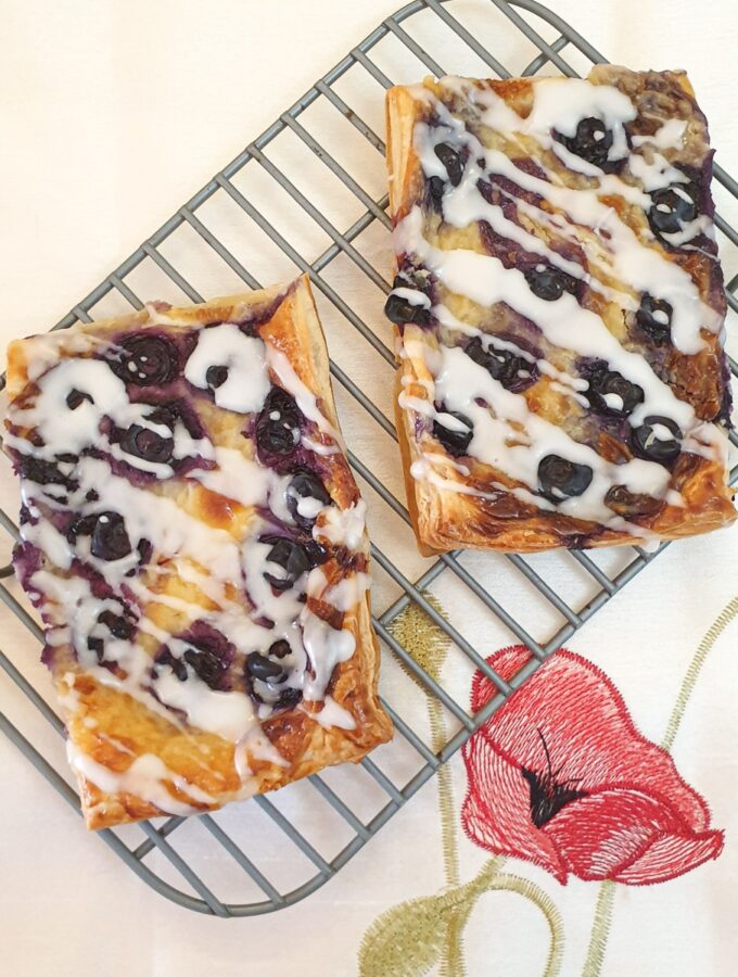2 blueberry cream cheese danish pastries drizzled with a sweet glaze on a cooling rack.