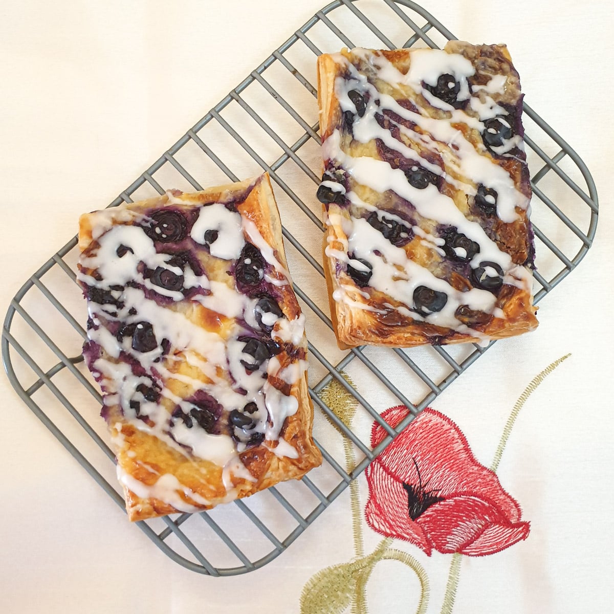 2 blueberry cream cheese danish pastries drizzled with a sweet glaze on a cooling rack.