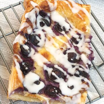 A blueberry cream cheese Danish pastry on a cooling rack.