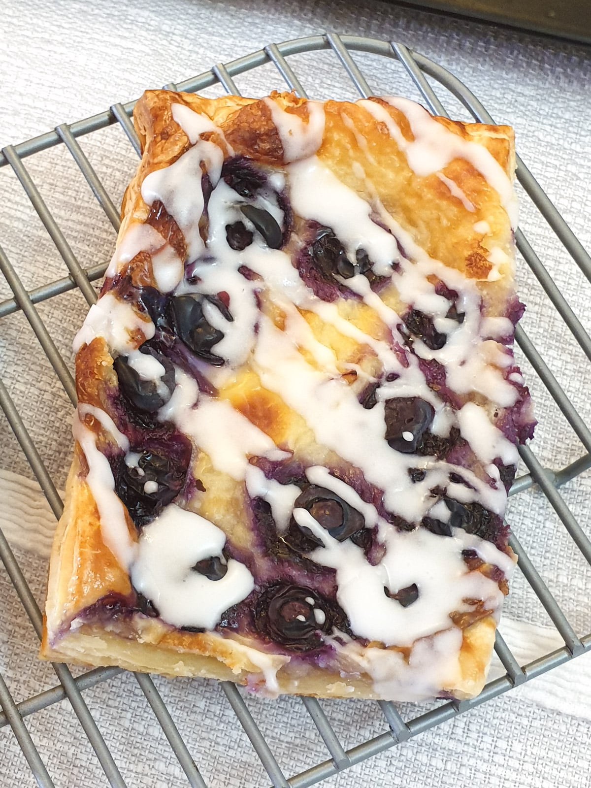 A blueberry cream cheese Danish pastry on a cooling rack.