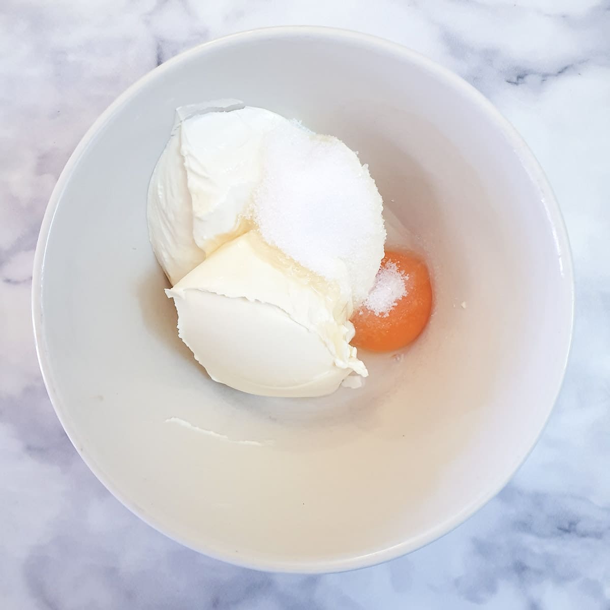 Mascarpone cheese, sugar and egg yolk in a mixing bowl.