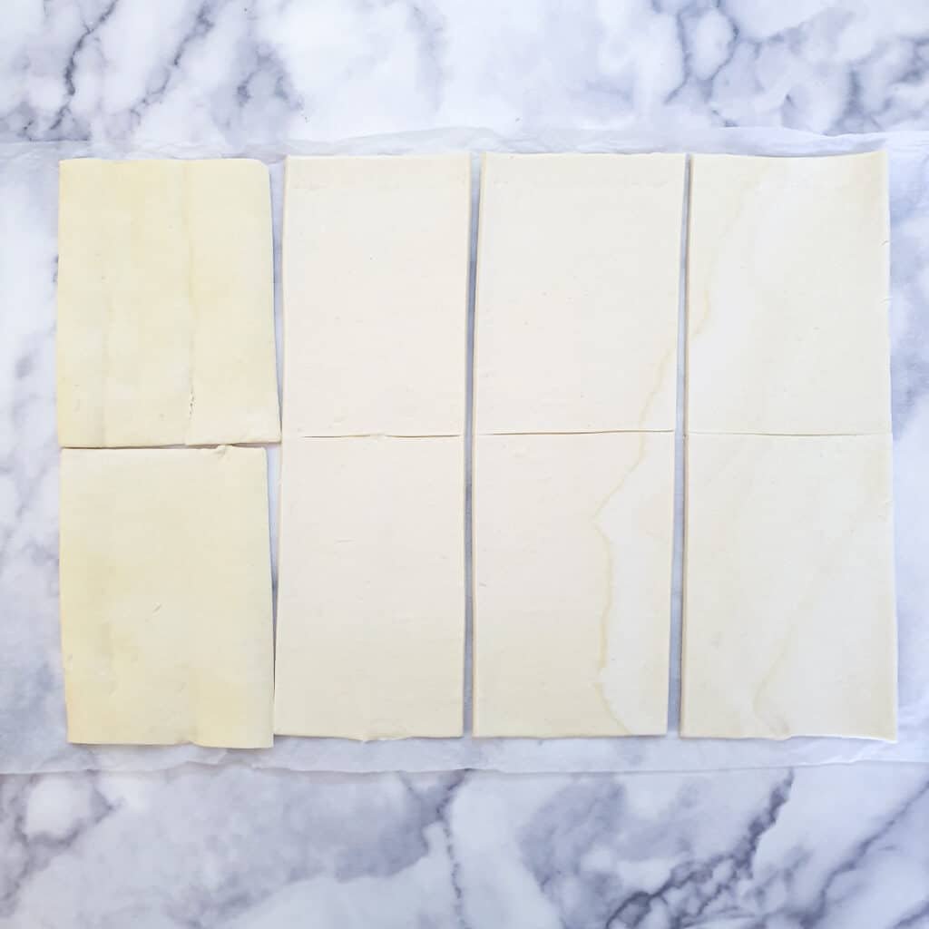 An unbaked roll of puff pastry unrolled on a table and cut into 8 rectangles.