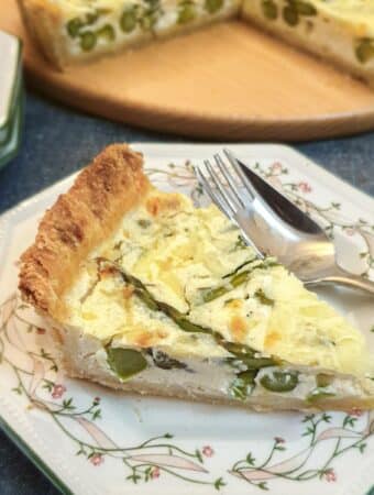 A slice of cheese and asparagus tart on a green patterned plate with a fork.