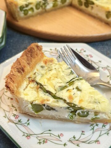 A slice of cheese and asparagus tart on a green patterned plate with a fork.