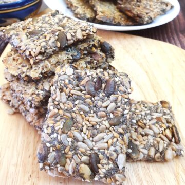 A pile of crispy seeded crackers on a wooden board.