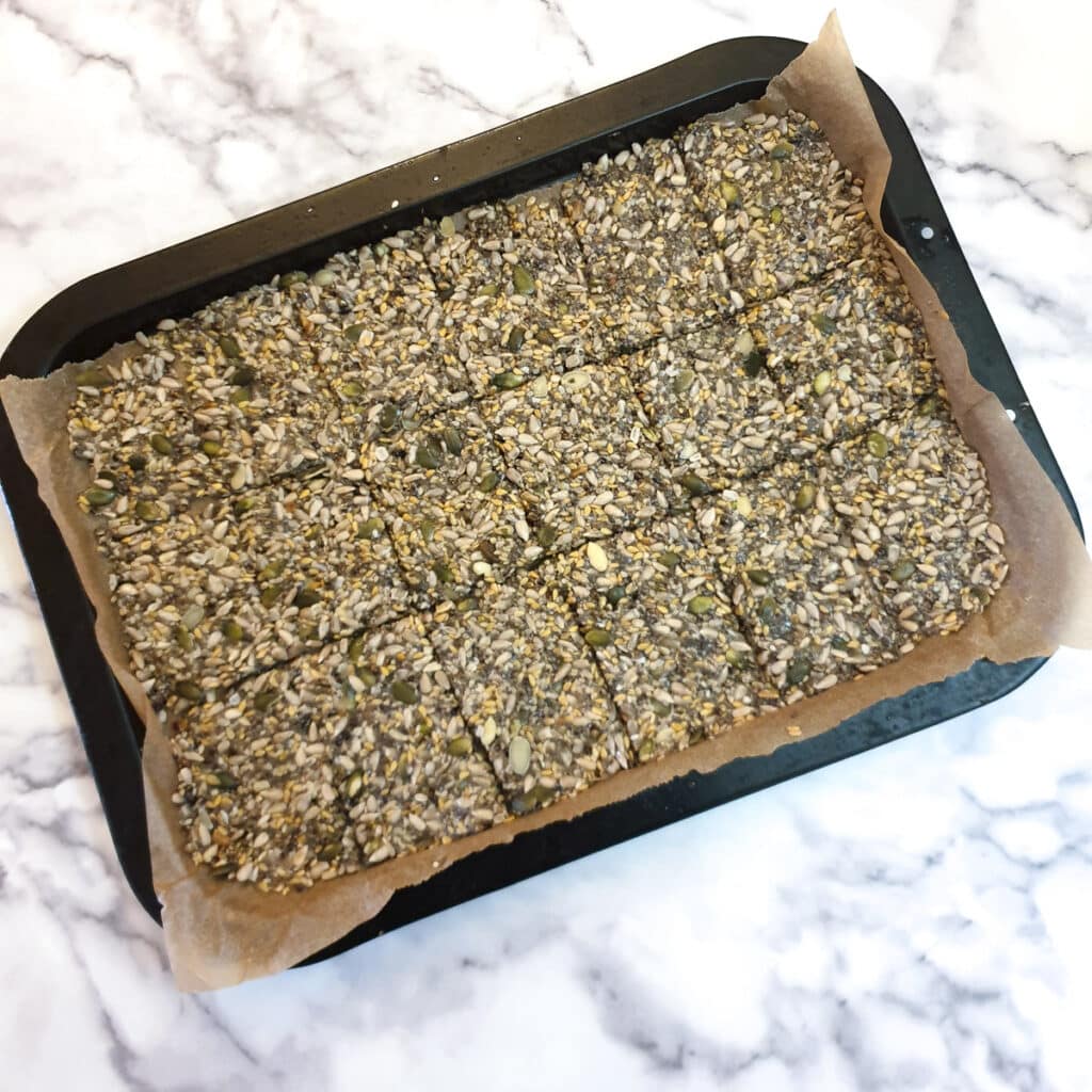 A baking tray with seeded crackers which have been scored to form squares.