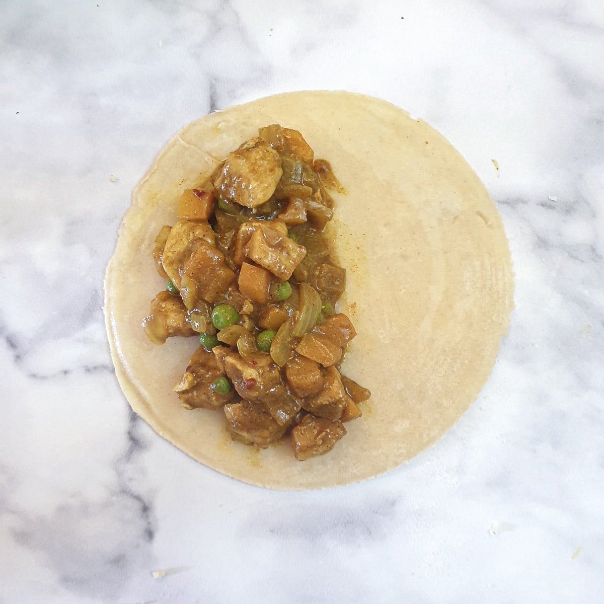 A circle of dough with a spoonful of curried chicken arranged on one half of the circle.