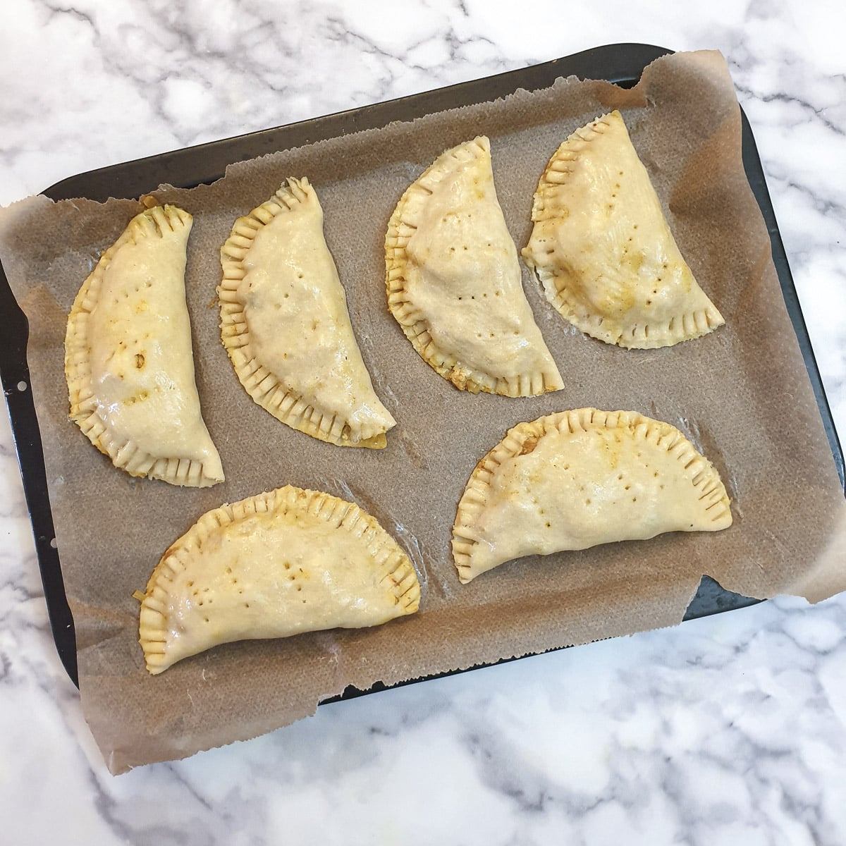 6 unbaked chicken curry pies on a baking tray.