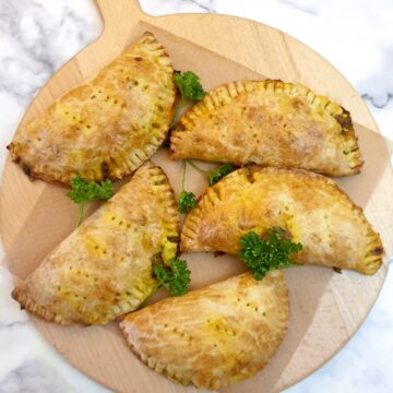 5 curried chicken pies on a round wooden board.