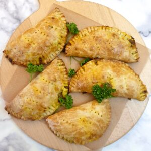 5 curried chicken pies on a round wooden board.