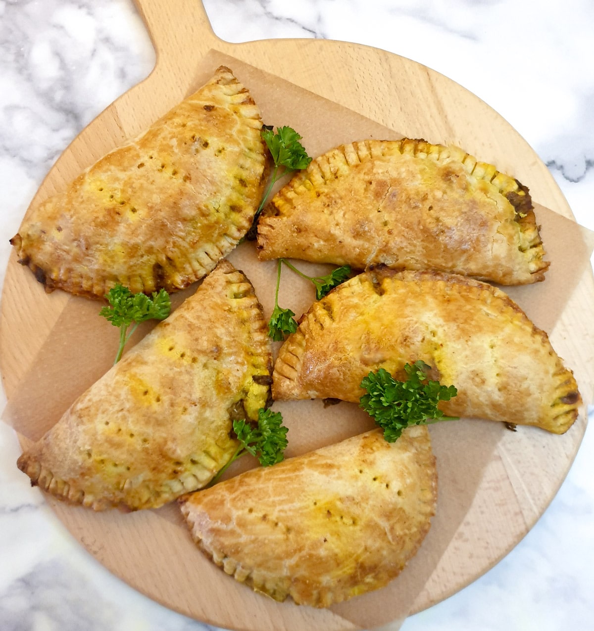 5 curried chicken pies on a round wooden board.