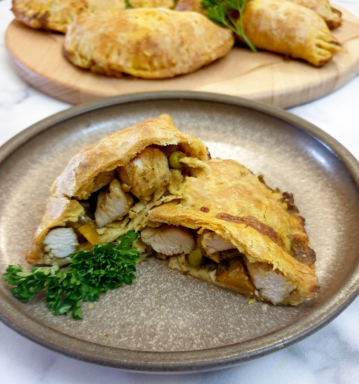 A curried chicken pie which has been cut in half to show the inside, arranged on a brown plate.