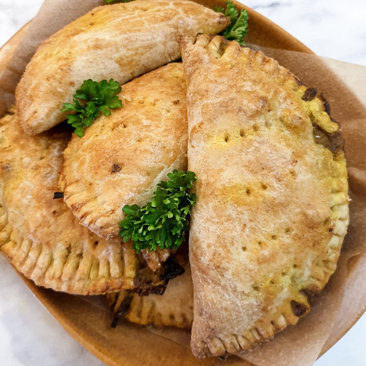 5 curried chicken pies on a pile on a brown plate.