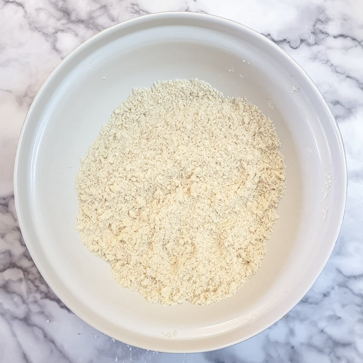 Flour and butter rubbed together to form 'breadcrumbs' in a mixing bowl.