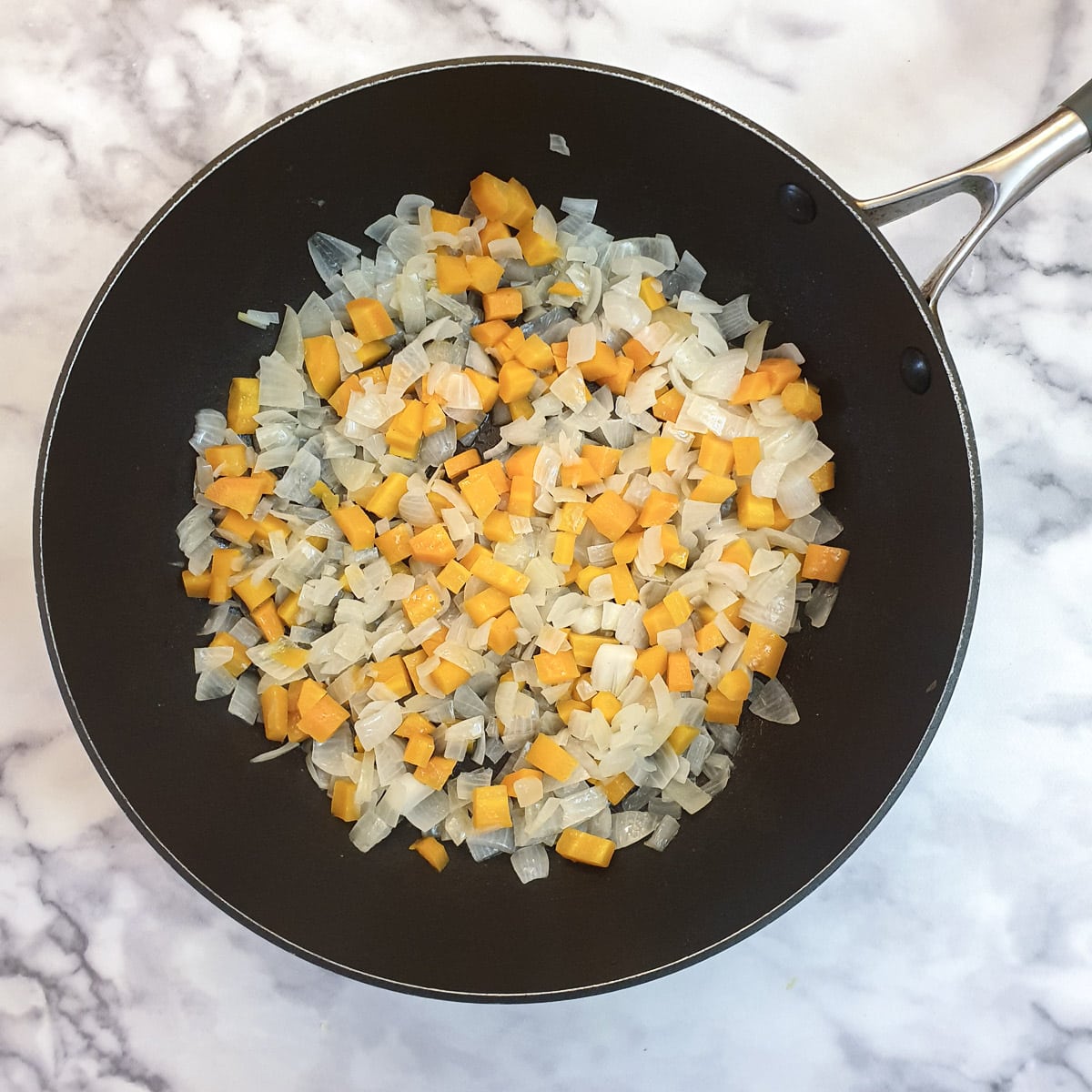 Finely diced onions and carrots in a frying pan.