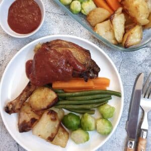 A duck leg smothered in plum sauce on a white plate with vegetables.