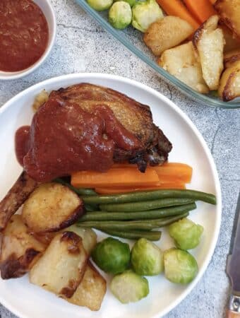 A duck leg smothered in plum sauce on a white plate with vegetables.