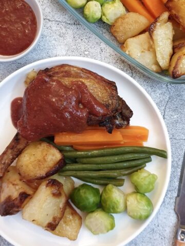 A duck leg smothered in plum sauce on a white plate with vegetables.