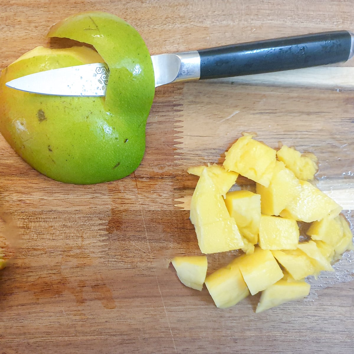 A slice of mango being peeled, next to a pile of mango cubes.